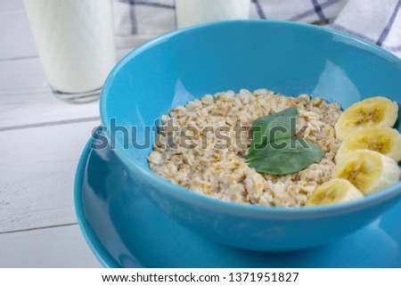 Plate with tasty oatmeal and banana slices on white wood background. Concept image of breakfast, healthy eating.