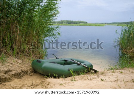 Rubber inflatable boat with oars is on the pier near the lake, surrounded by reeds. There is not anyone. Overcast weather