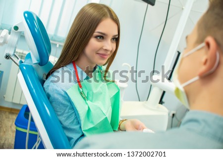 A beautiful girl is sitting in the dental chair and looking at a man doctor who is talking to her. dental clinic Royalty-Free Stock Photo #1372002701