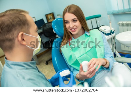 A beautiful girl is sitting in the dental chair and looking at a man doctor who is talking to her. dental clinic Royalty-Free Stock Photo #1372002704