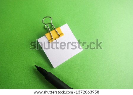 Pen, yellow paper clip and blank paper on a green background