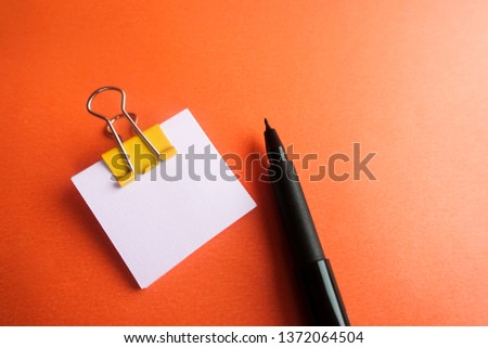 Pen, yellow paper clip and blank paper on a orange background