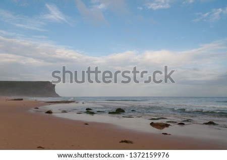 Empty beach with yellow sand, mild waves and cliff in the distance. Garie Beach in Royal National Park, NSW, Australia