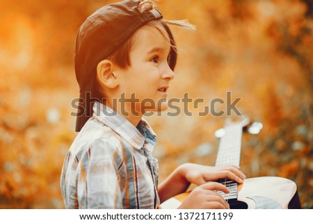Child in a autumn park. Little boy in a shirt. Kid with a guitar