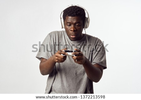 Man of African appearance with earphones and a gamepad in his hands playing a video game console