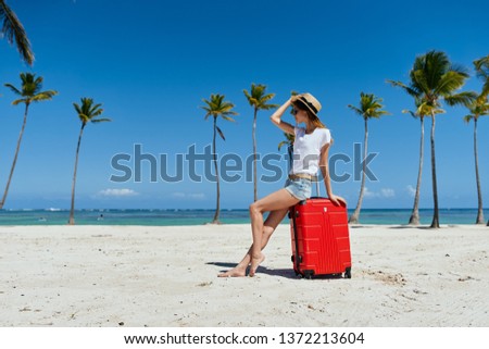 Pretty woman sitting on a red suitcase on the beach white sand island relax