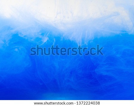 Blue paint dissolved into water, close up view. Abstract background. Abstract pattern of ink dissolving into water. Acrylic paint swirling in liquid. Drop of ink in liquid. Blurred background