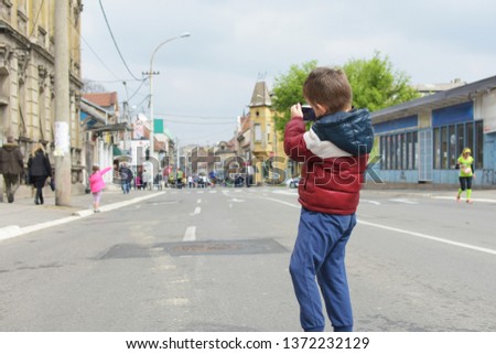 Small boy photographer in a pose for shooting photos preparing to photograph the oncoming marathon runners. 