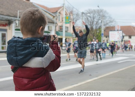 A runner holds his hands high in front of a kid photographer during a Belgrade marathon race. 