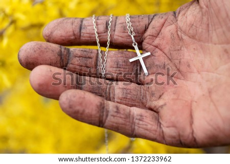 Silver cross in the dirty hand of a male tramp.