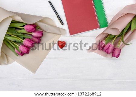 Notepad with heart and bouquet of tulips on white wooden table