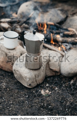 Closeup photo of white cup and coffee maker near to bonfire. Concept adventure active vacations outdoor. Summer camp