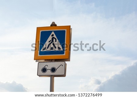 Road sign - Pedestrian crossing. Square blue and white metal plate with white stripes and a walking man and reflective yellow margins. Transition for the blind with an audible alert. 