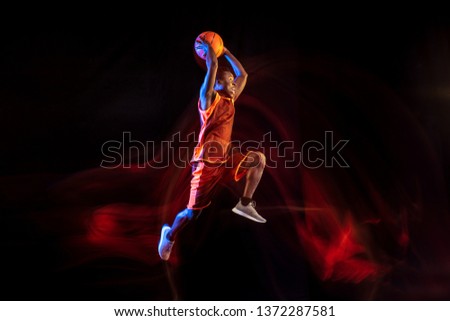 One step higher. African-american young basketball player of red team in action and neon lights over dark studio background. Concept of sport, movement, energy and dynamic, healthy lifestyle.