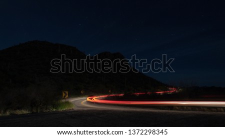 Trails of light from passing vehicles driving through Saguaro National Park at Contzen Pass on Picture Rocks Road. Sonoran Desert landscape at night, just before dawn. Pima County, Tucson, Arizona. 