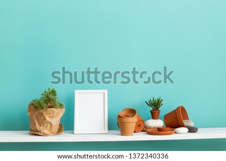Modern room decoration with picture frame mockup. White shelf against pastel turquoise wall with pottery and succulent plant with potted succulent plant.