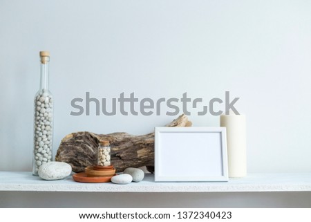 Modern room decoration with picture frame mockup. Shelf against white wall with decorative candle, glass and rocks.
