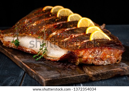 Baked Halibut fish with lemon on wooden board on dark background, hot smoked seafood