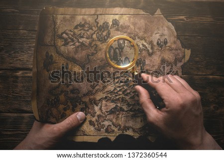 Traveler is looking on an old map in his hands through a magnifying glass. Treasure hunt concept.o