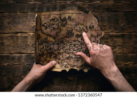 Old map in man adventurer hands on a brown table background. Treasure hunt concept.