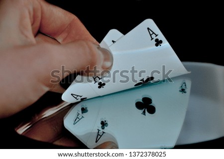 Playing poker. Cards reflect from shiny table and black background. Two aces in hand. Gambling addiction.