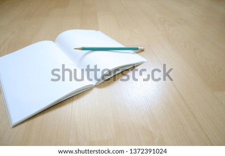 The white plain notebook and pencil on the wooden floor. Copy spcae for editing. Abstract image. Wallpaper image.