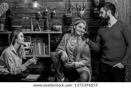 Friends, family spend pleasant evening, interior background. Girls and man on happy faces hold metallic mugs, enjoy coziness with drinks. Coziness concept. Friends drinking tea and chatting.