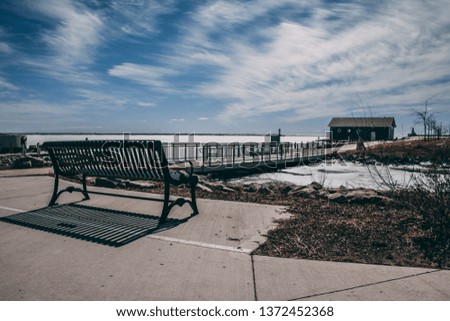 Beautiful views from port Stanley harbor; Metal park bench looking out over frozen lake Erie; Concrete walking path in the distance with a bridge; Ontario Canada