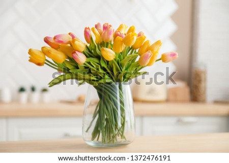 Close-up of a bouquet of fresh spring yellow tulips in a large transparent glass vase in a photo studio against the background of a beautiful kitchen. Concept photography for a flower shop