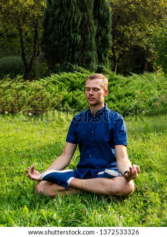 The guy is sitting on the grass in the lotus position