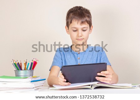 Kid sitting at table with books notebooks and using tablet computer