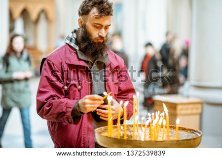 Bearded man putting candles while praying in the church
