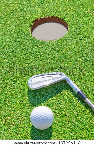 Golf putter ball near the hole in the vertical format. Against the background of grass.