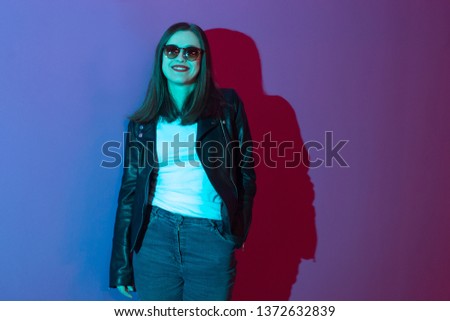 Fashioned girl in leather jacket in dark glasses in pink anf blue  neon lights background. 