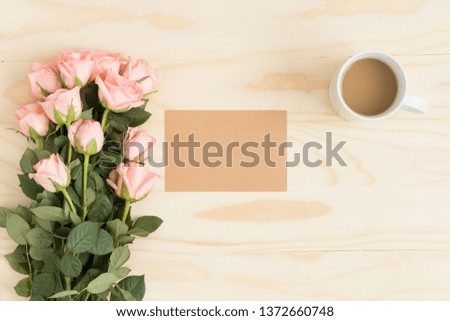 Top view of a kraft card mockup with a bouquet of pink roses and a coffee on a wooden table.