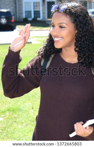 College student on her way to school carrying a book while waving at a friend. Royalty-Free Stock Photo #1372665803