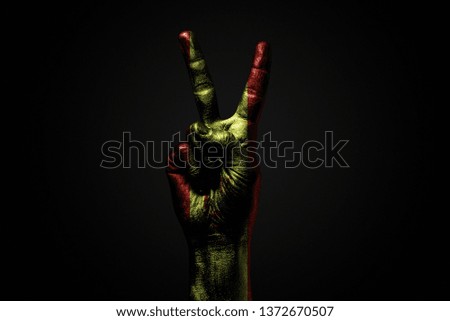 A hand with a drawn Spain flag shows an PEACE sign, a symbol of peace, friendship, greetings and peacefulness on a dark background. Horizontal frame