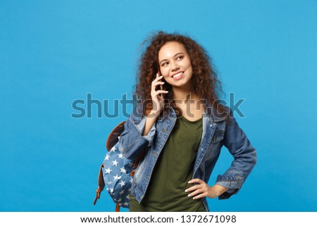 Young african american girl teen student in denim clothes, backpack hold phone isolated on blue background studio portrait. Education in high school university college concept. Mock up copy space