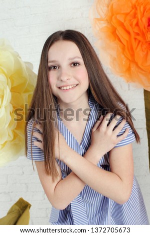 Beautiful teen girl posing in studio with artificial big flowers