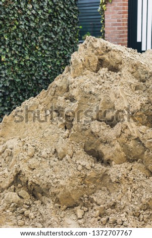 Heap of sand in front of hedge and a wall