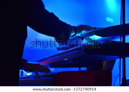 Hands of an artist playing on stage synthesisers in a heavily blurred environment of a music studio.  Royalty-Free Stock Photo #1372740914