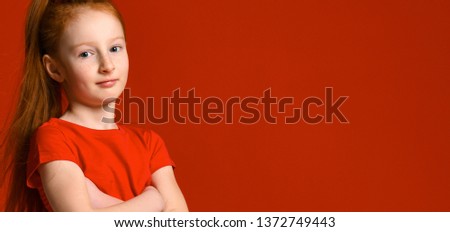 Portrait of a young gentle redhead teenage girl with healthy freckled skin, wearing a red tank top, looking at the camera with a serious or pensive expression.