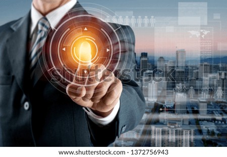 Businessman with a glowing finger pointing at HUD and infographics, data. Blurred blue background. Toned image double exposure urban city background,copy space.
  
