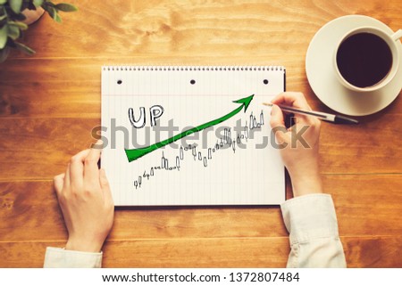 Market up trend chart with a person holding a pen on a wooden desk