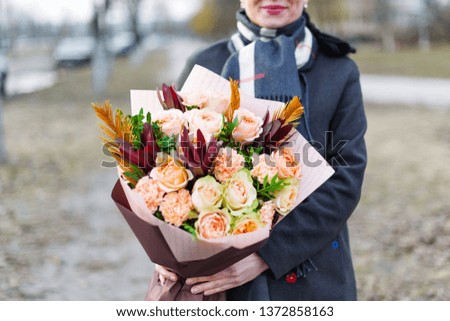 Woman in coat holding a cute bunch of beautiful roses in paper. Closeup photo