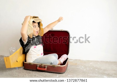Cute Asian girls are enjoying playing as imagined, Is traveling to her dream by sitting in a suitcase. There is a helmet and jets wings made of crate paper. white background.
