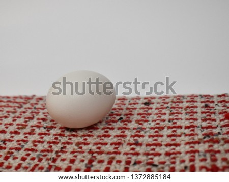 Single white egg on red and white hand woven cloth, with a white background, Low angle, close up picture.  Natural, organic, healthy food, dignified. 