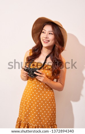 Attractive young woman with a photo camera in her hand on an isolated beige background. The concept travel