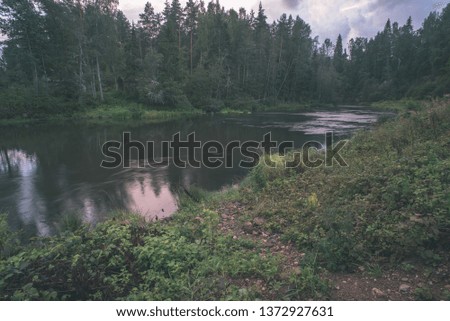blue sky white clouds over calm body of water in summer with green foliage, trees and grass on the shores - vintage retro look