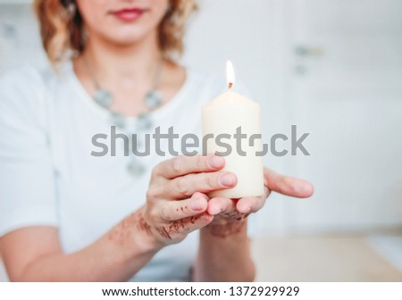 Blonde young woman in white clothing with mehendi holding burning candle